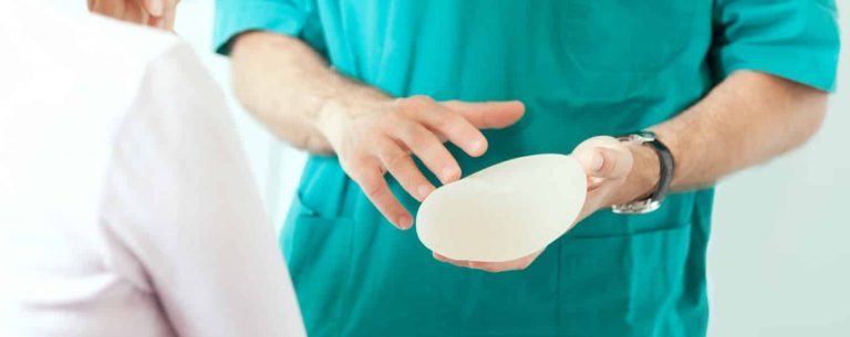 A plastic surgeon holding a breast implant, representing breast explant surgery