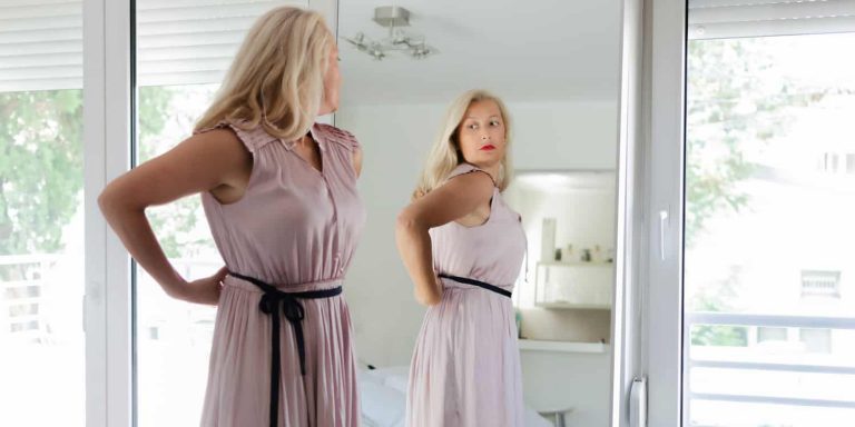 A woman looking in the mirror, representing the link between plastic surgery and body image