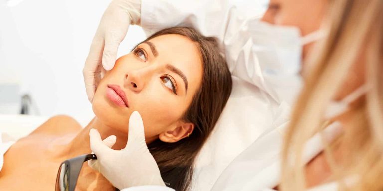 A surgeon examining a woman's face during a plastic surgery consultation