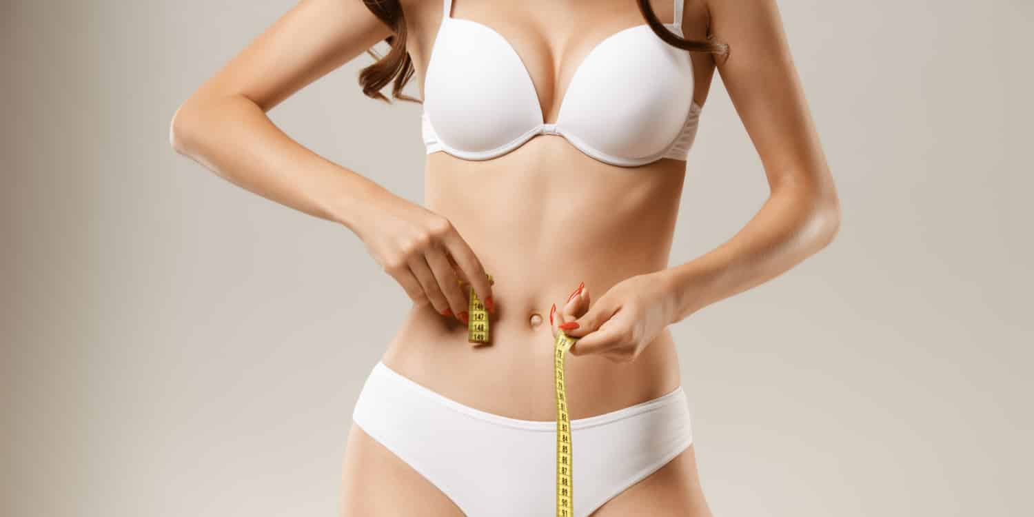 A woman measuring her waist and wondering "is liposuction permanent?"