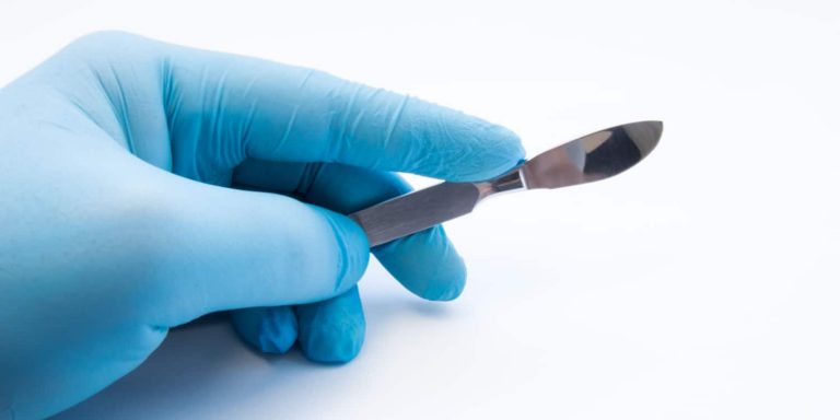 A gloved hand holding a scalpel for cosmetic surgery